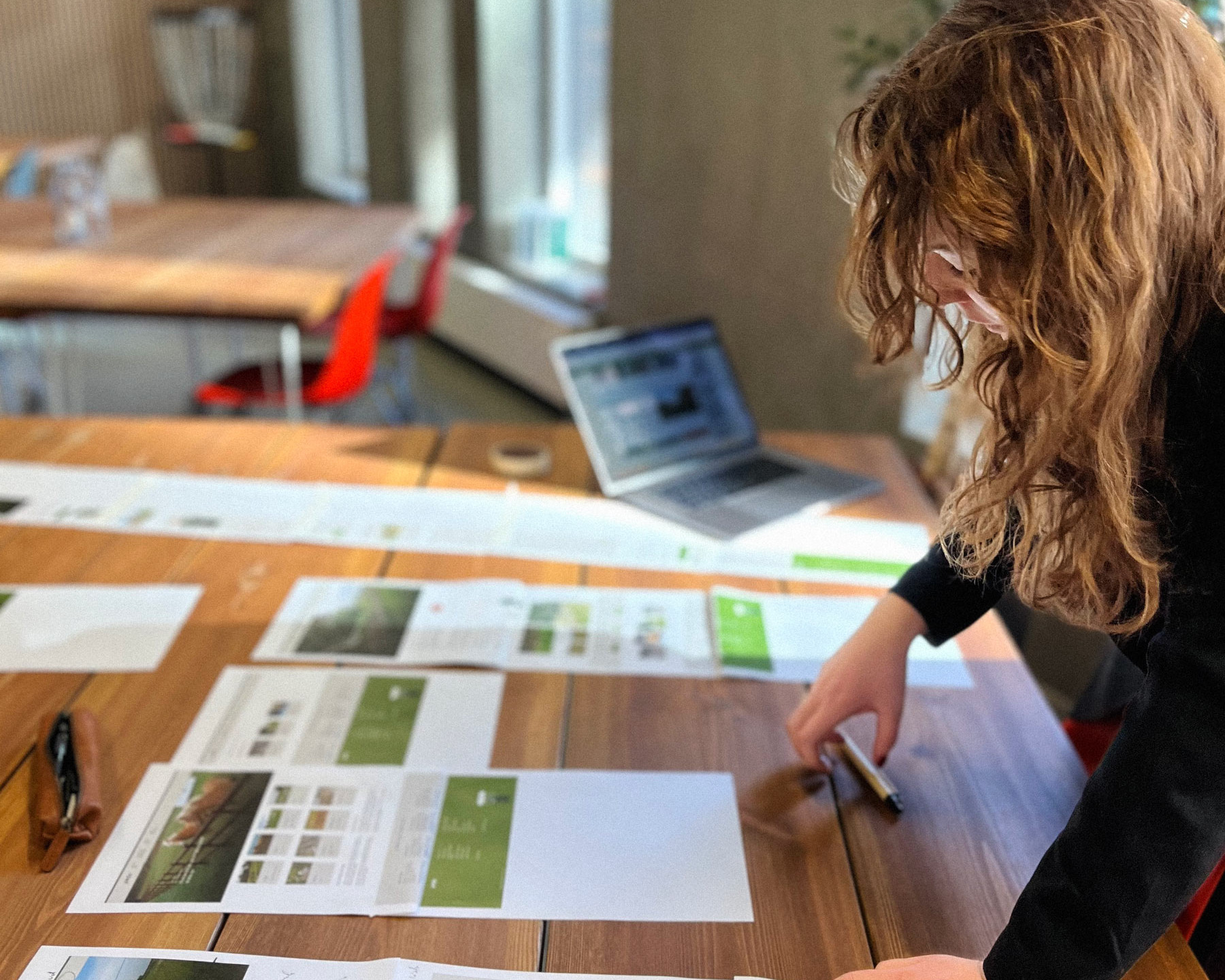 Et billede af en kvinde der står ved et skrivebord og arbejder med udprintede versioner af et website