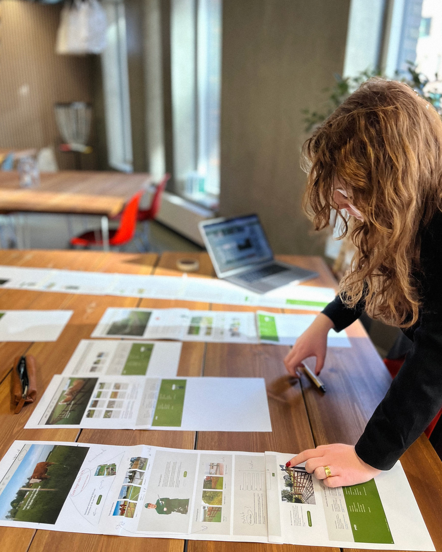 Et billede af en kvinde der står ved et skrivebord og arbejder med udprintede versioner af et website