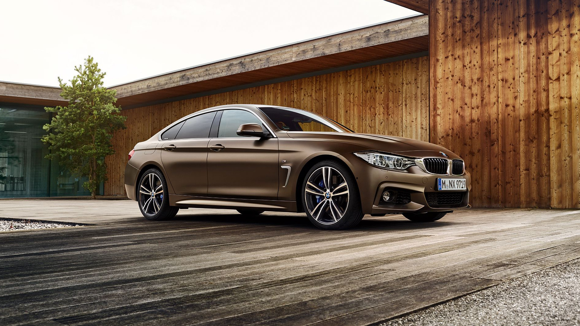 En brun BMW parkeret foran en moderne bygning med træpaneler.
