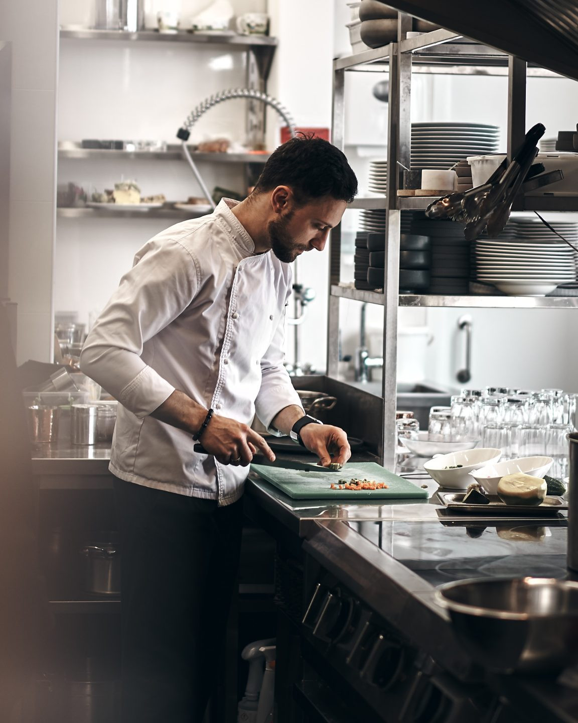 En kok iført hvid jakke skærer ingredienser på et skærebræt i et professionelt køkken