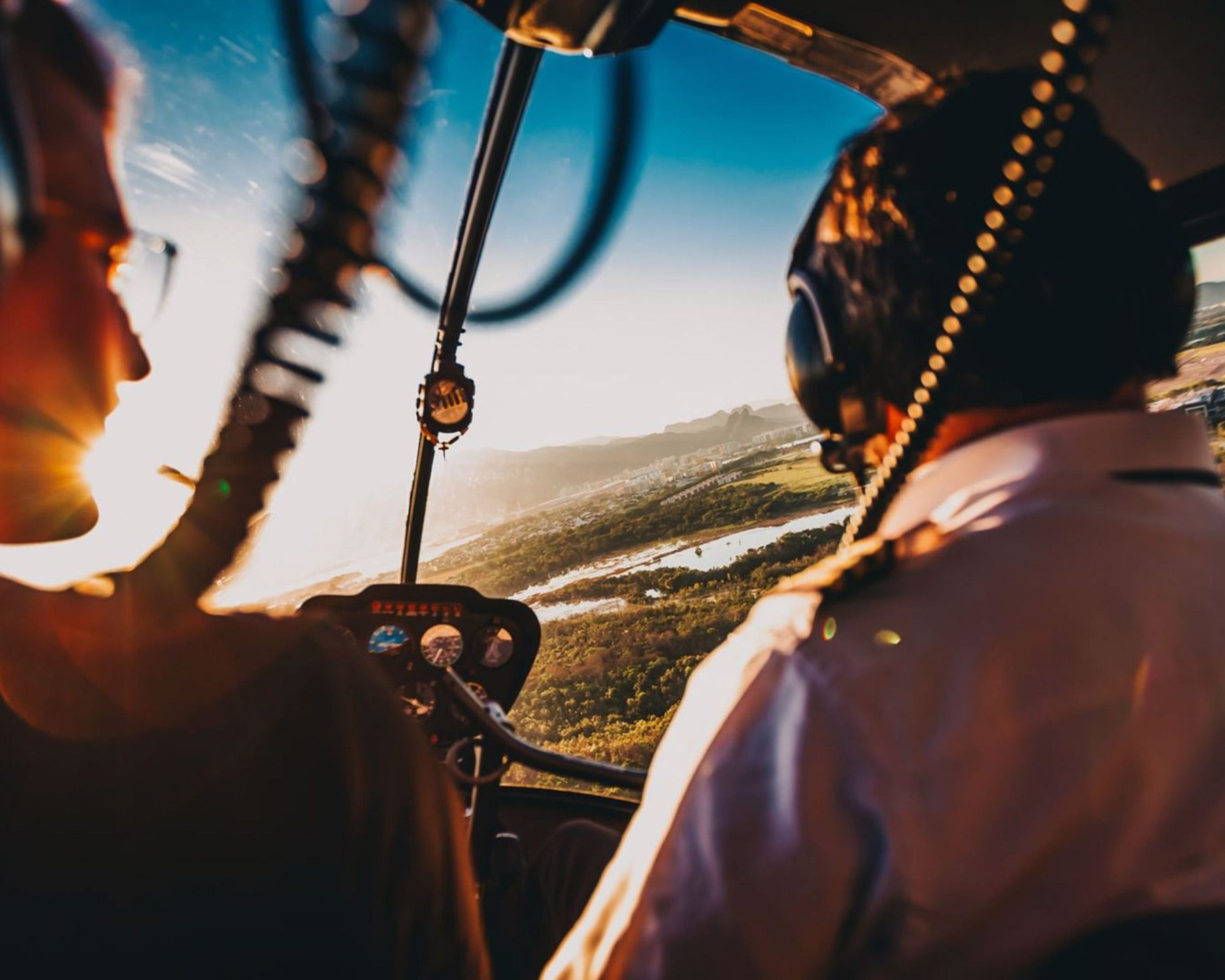 Billede af to piloter i en helikopter, der flyver over et naturskønt landskab