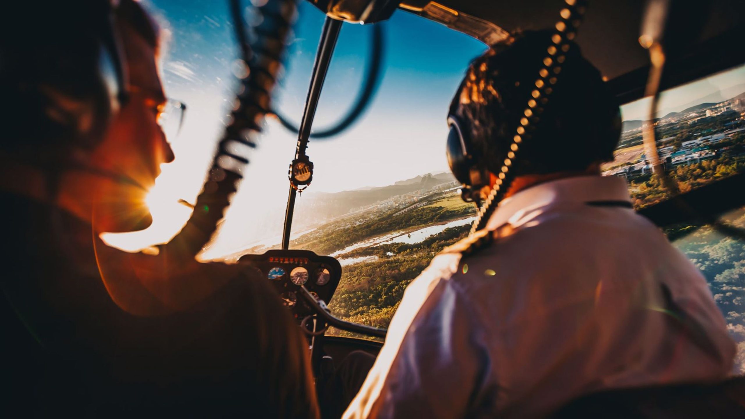 Billede af to piloter i en helikopter, der flyver over et naturskønt landskab