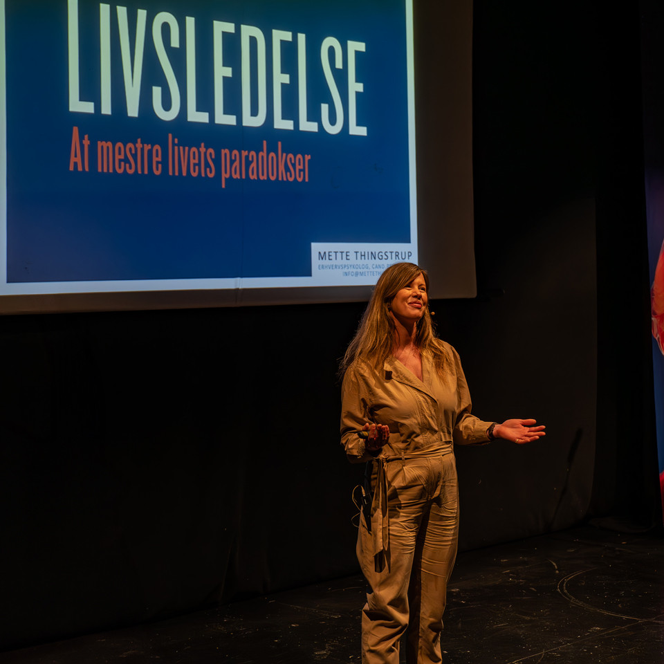 En kvinde holder et foredrag foran en stor skærm med titlen
