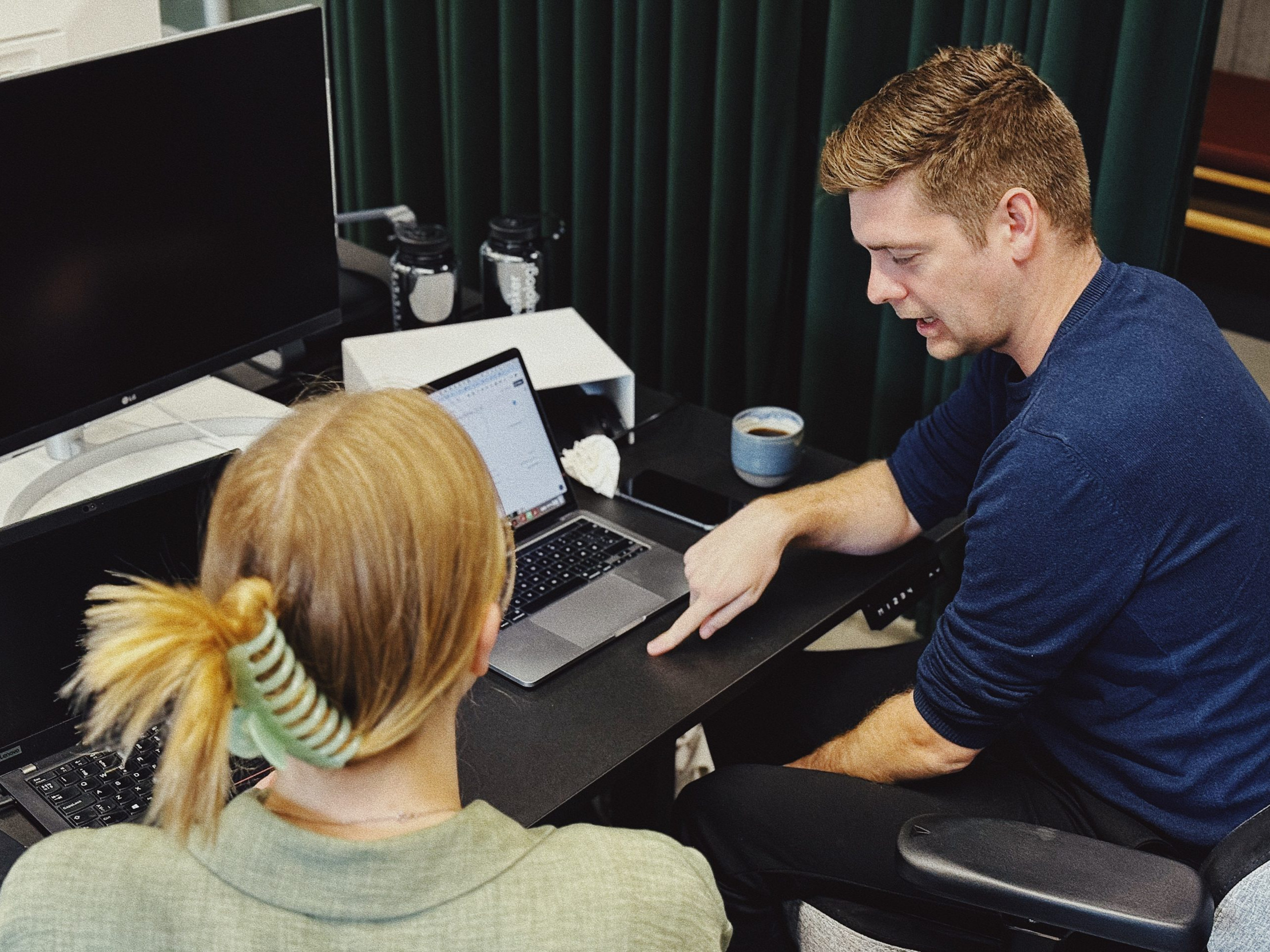 To personer i samtale på kontor med bærbar computer og kaffekop ved siden af.
